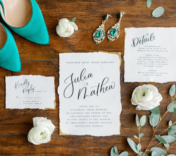 wedding invitations on a table with earrings, shoes, and flowers