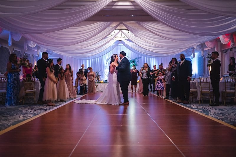 bride and groom enjoying first dance on large dance floor while guests watch and take video, photo taken by Nativ Lens