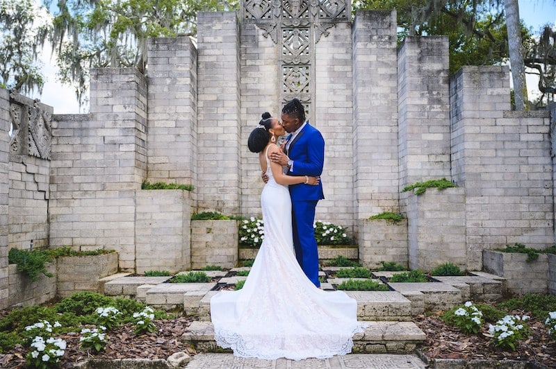 bride and groom kissing outside in a garden with a large stone structure, photo taken by Nativ Lens