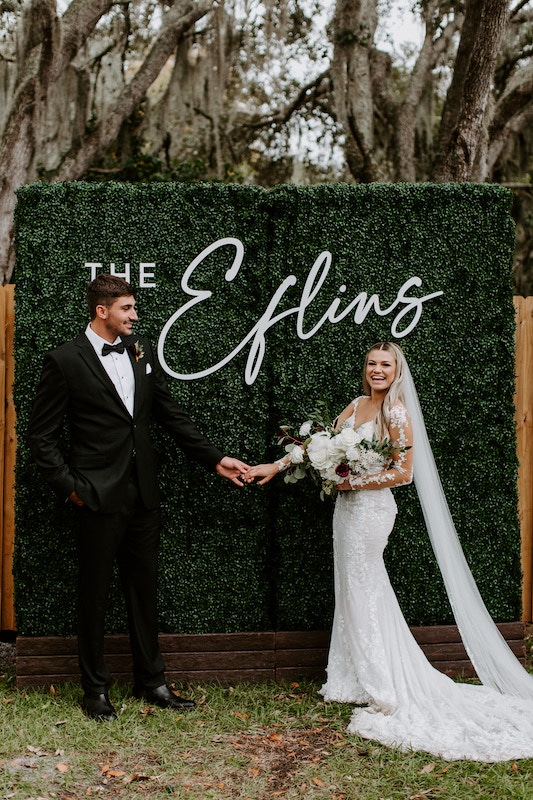 bride and groom standing in front of green wall with their name on it