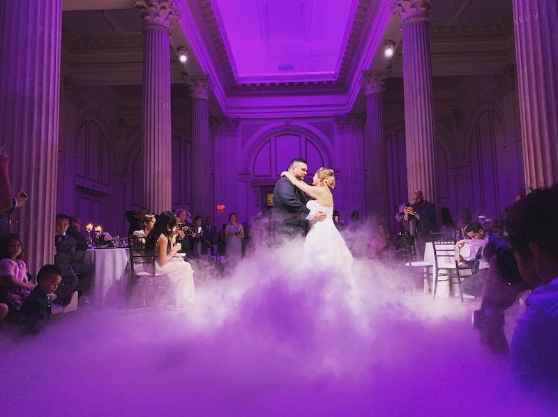 bride and groom enjoying first dance on floor with fog and purple lighting
