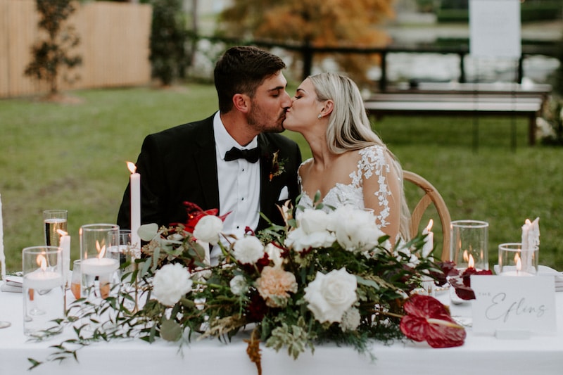 bride and groom sitting at sweetheart table for outdoor reception and kissing