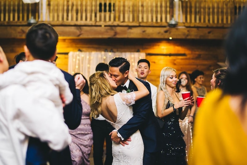 bride and groom kissing each other on dance floor surrounded by friends and family
