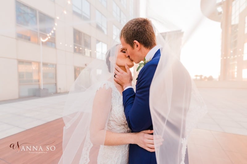 bride and groom kissing while brides veil floats on the wind around them