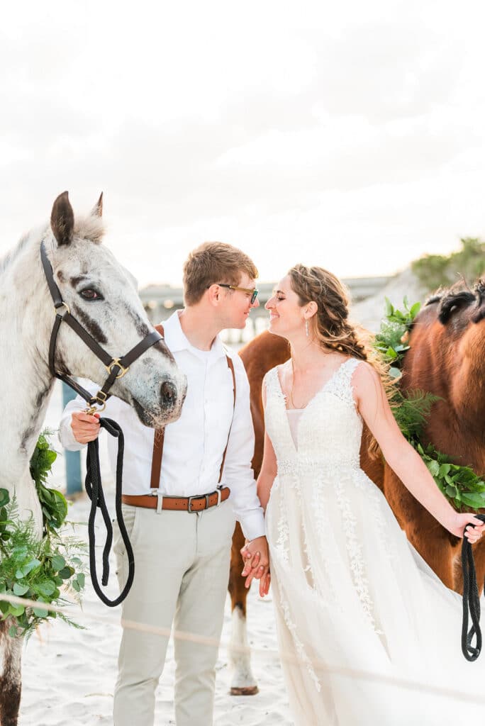 bride and groom looking into each other's eyes while holding on to their horses