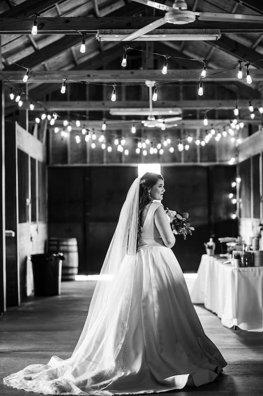 black and white image of a bride standing in a barn in her wedding dress, SMO Photography