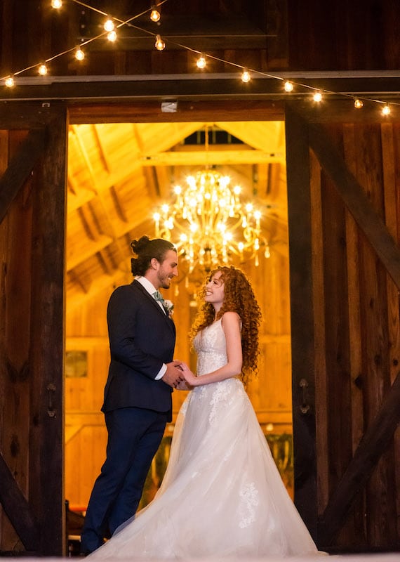 bride and groom holding hands while standing in front of open barn doors at night, SMO Photography