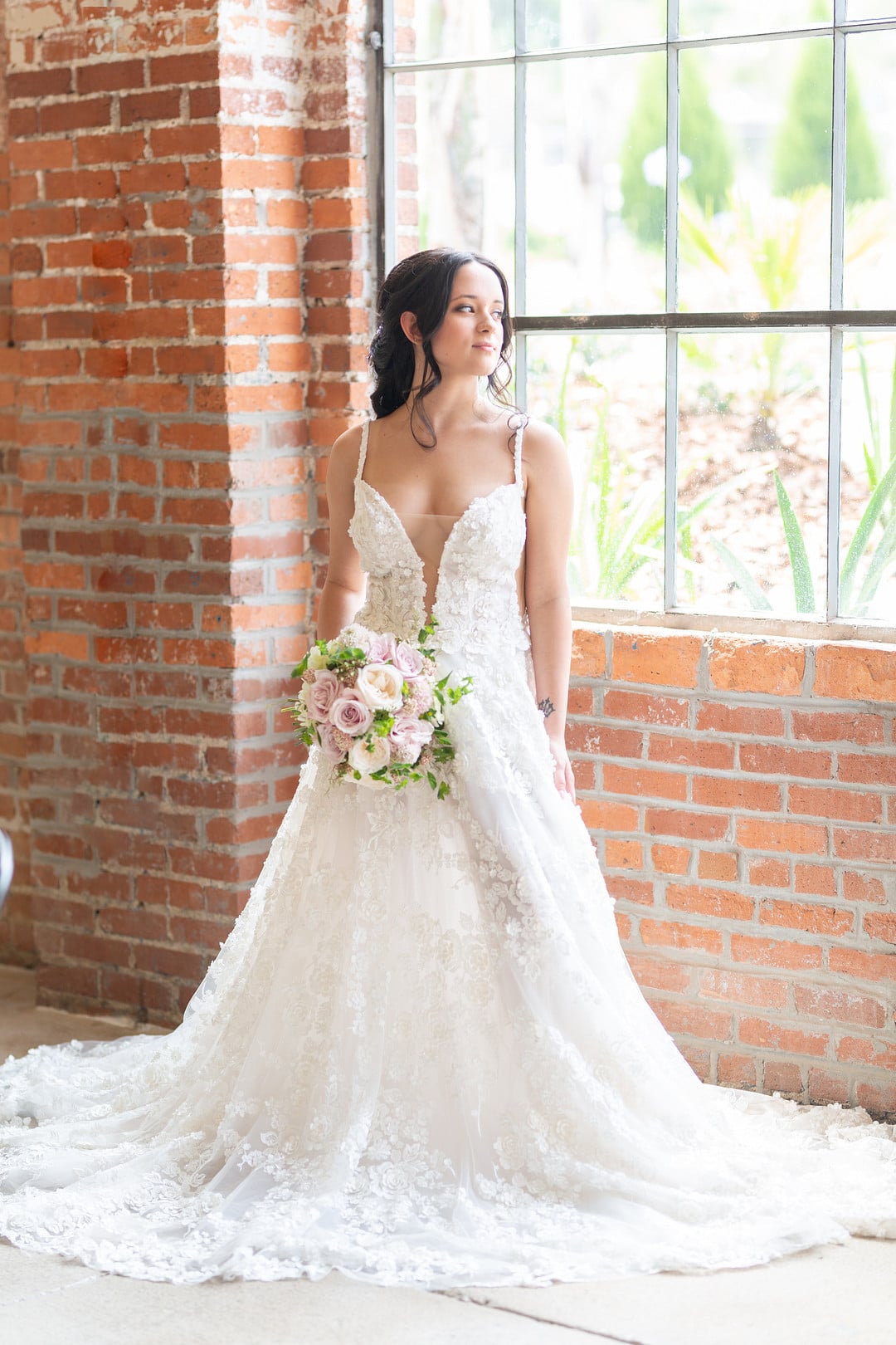 bride with a bouquet of flowers looking out the large windows with surrounding brick