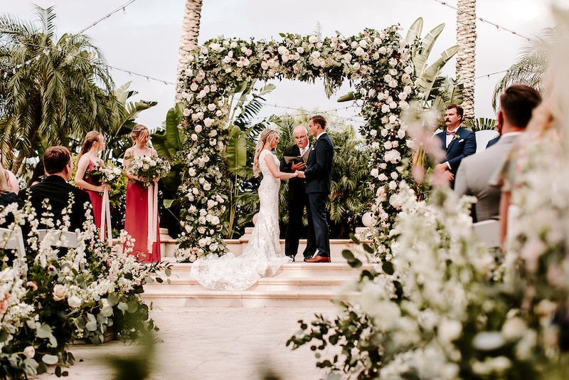 wedding ceremony outdoors with flowers setup along the seats and the archway