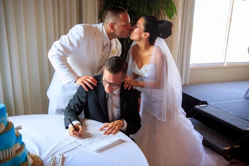 bride and groom kissing while Sam from Weddings By Sam signs the marriage certificate