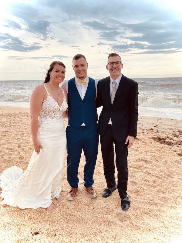 bride and groom standing on beach with Sam from Weddings By Sam
