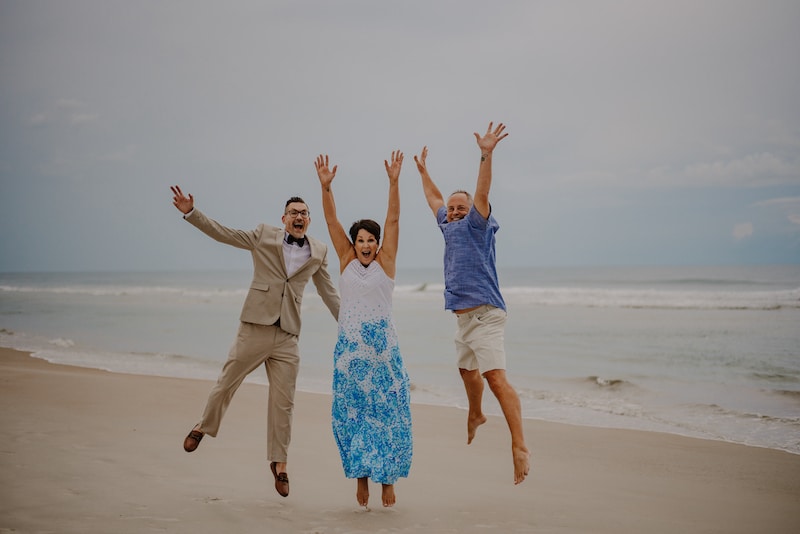 Sam from Weddings By Sam jumping on a beach with bride and groom