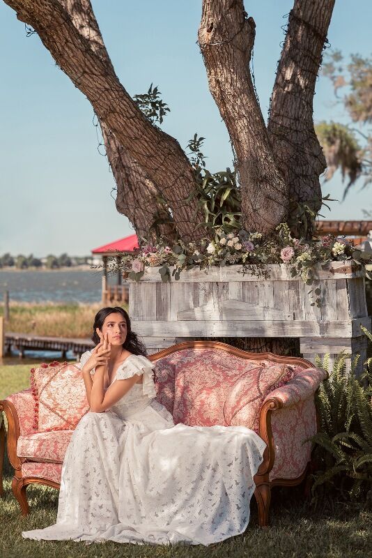 woman in a white wedding dress sitting on a pink love seat under a large tree