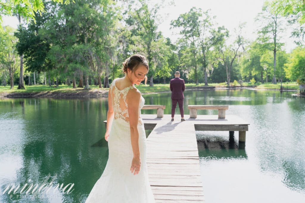 groom standing on end of dock with bride walking to him from behind