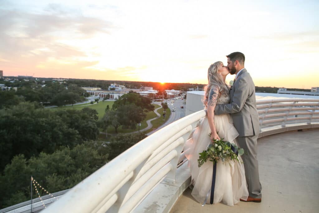 bride and groom kissing on a balcony as the sun sets in the distance