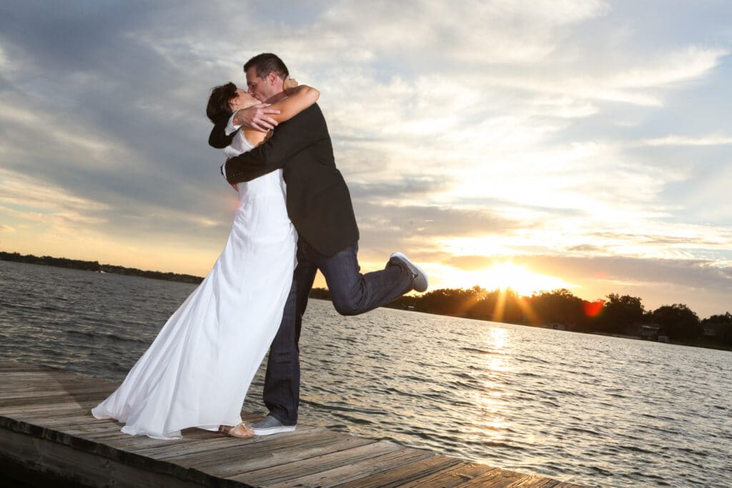 bride and groom kissing on a dock as the sun sets behind them