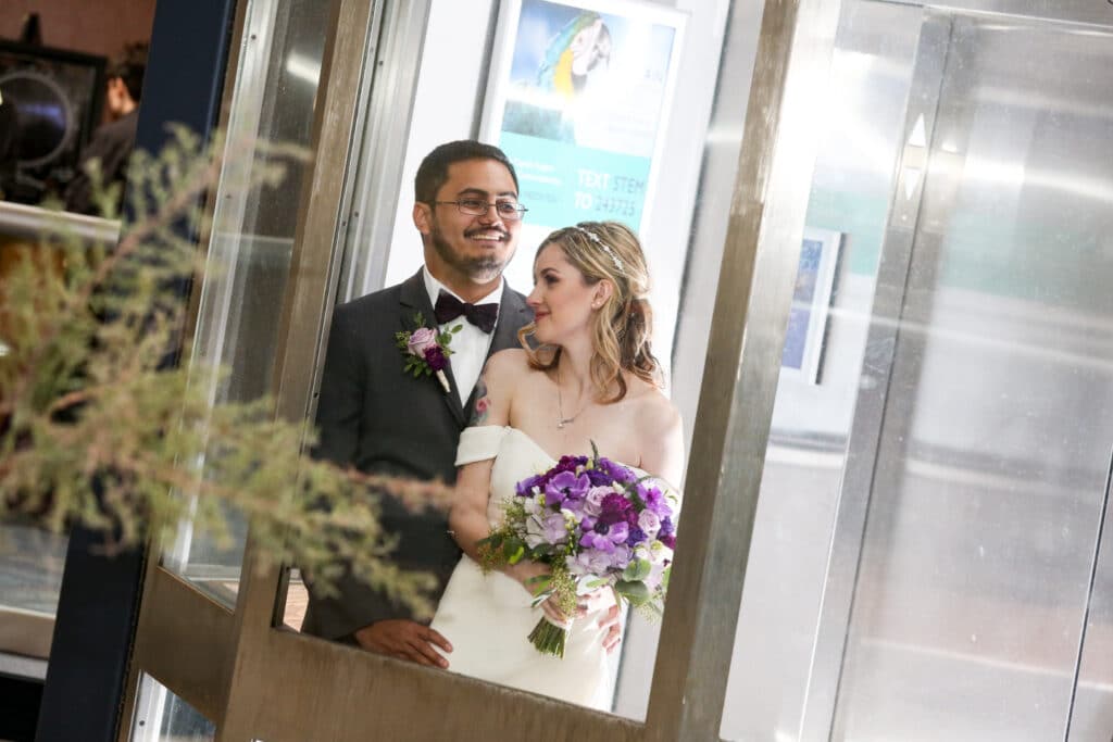 bride and groom standing in elevator with glass walls