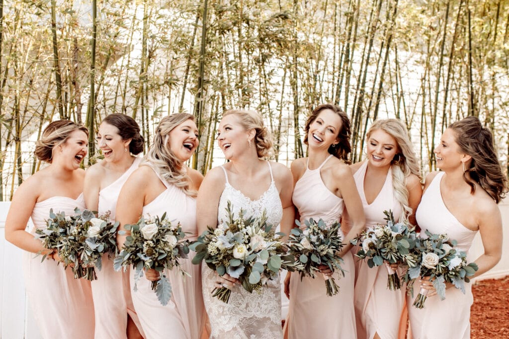 bride and bridesmaids laughing while holding flower bouquets