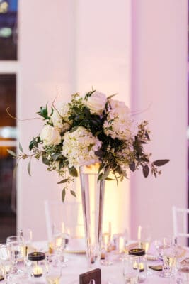white floral arrangement in tall glass vase on white table