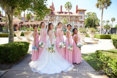 bride with bridesmaids in long pink dresses in front of spanish style building with palm trees