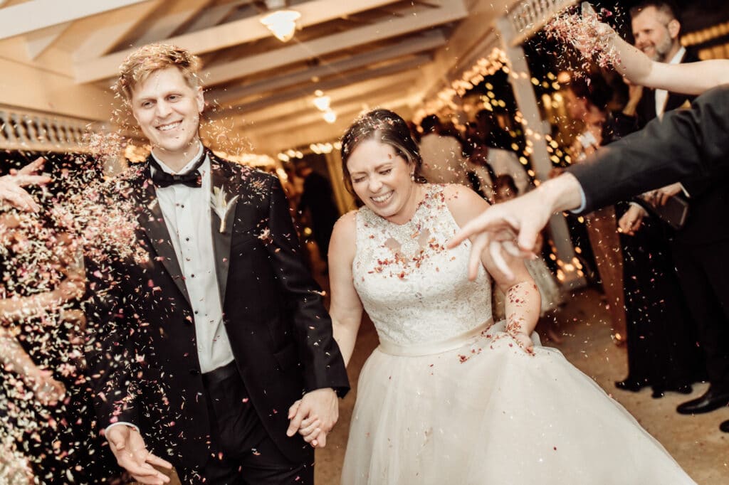 bride and groom getting covered with confetti tossed by wedding guests