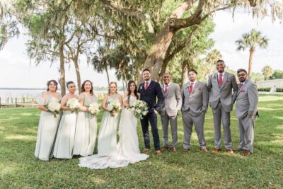 bride and groom with bridal party standing under large oak tree in front of lake