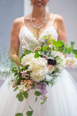 bride holding large bouquet with big white flowers, small pink and purple flowers and cascading leaves