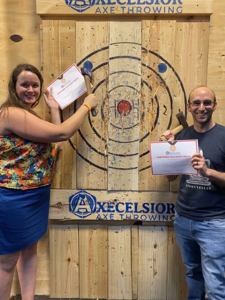 man and woman holding axes next to wooden target at Axecelsior Axe Throwing