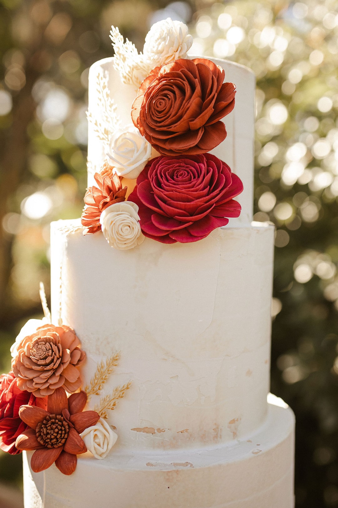 the 3 tier white cake with red, orange and white wooden flowers for the central florida boho wedding inspiration