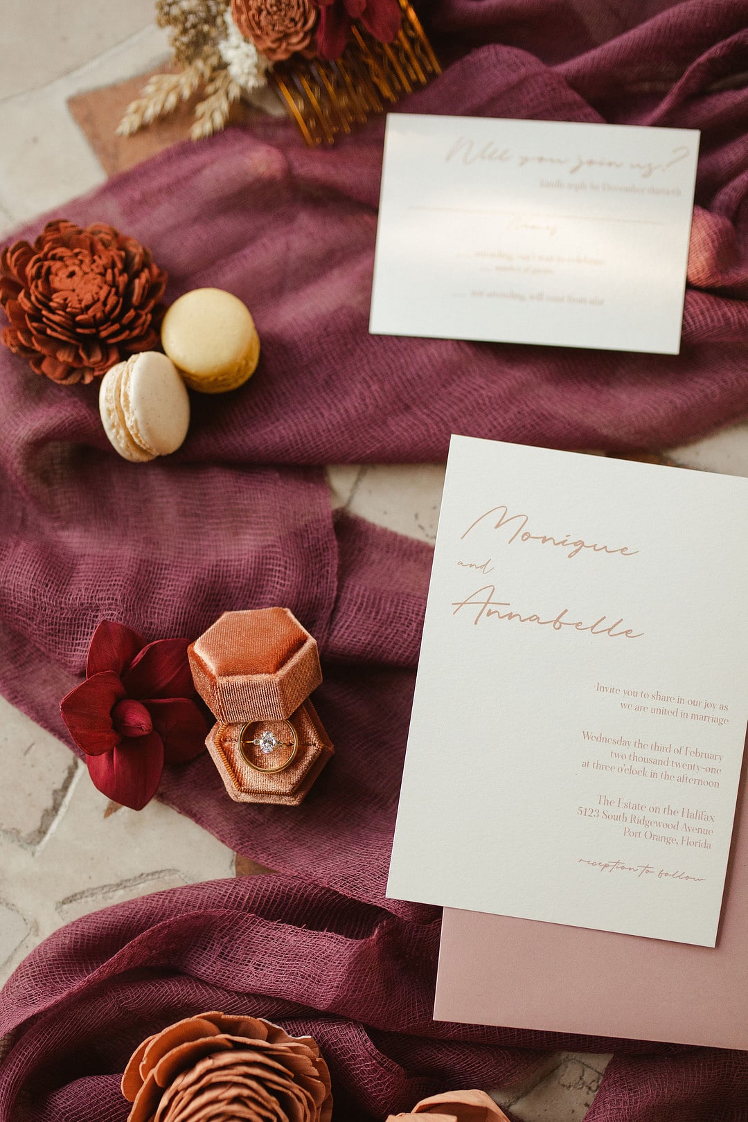 a close up photo of the invitation on a burgundy cloth with wooden flowers surrounding
