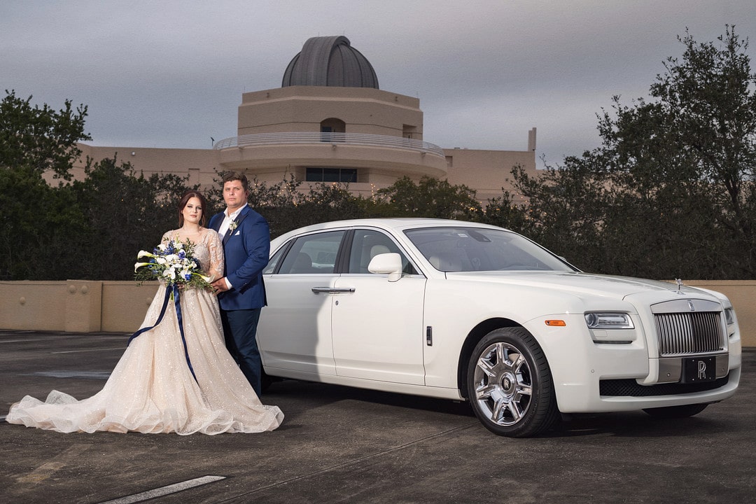 bride and groom standing next to their limo in the parking lot