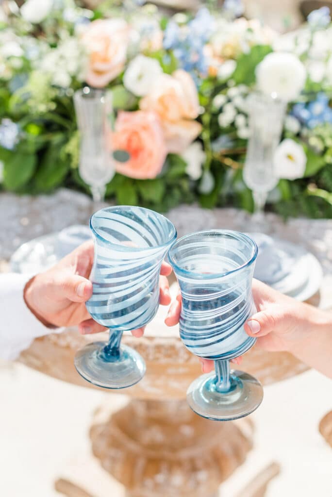 two blue glasses being held together by the bride and groom