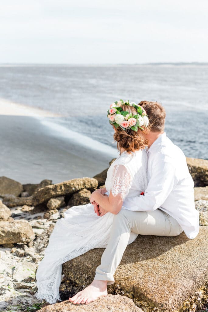 bride and groom sitting on a rock looking over the beach