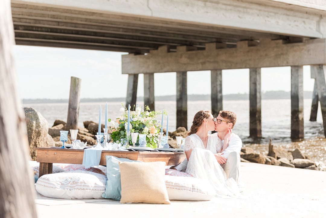 bride and groom sitting next to their reception table kissing for the amelia island beach wedding inspiration shoot