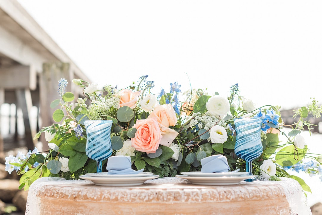 the sweethearts table with blue, pink, and whit florals and two blue glasses next to stacks of plates