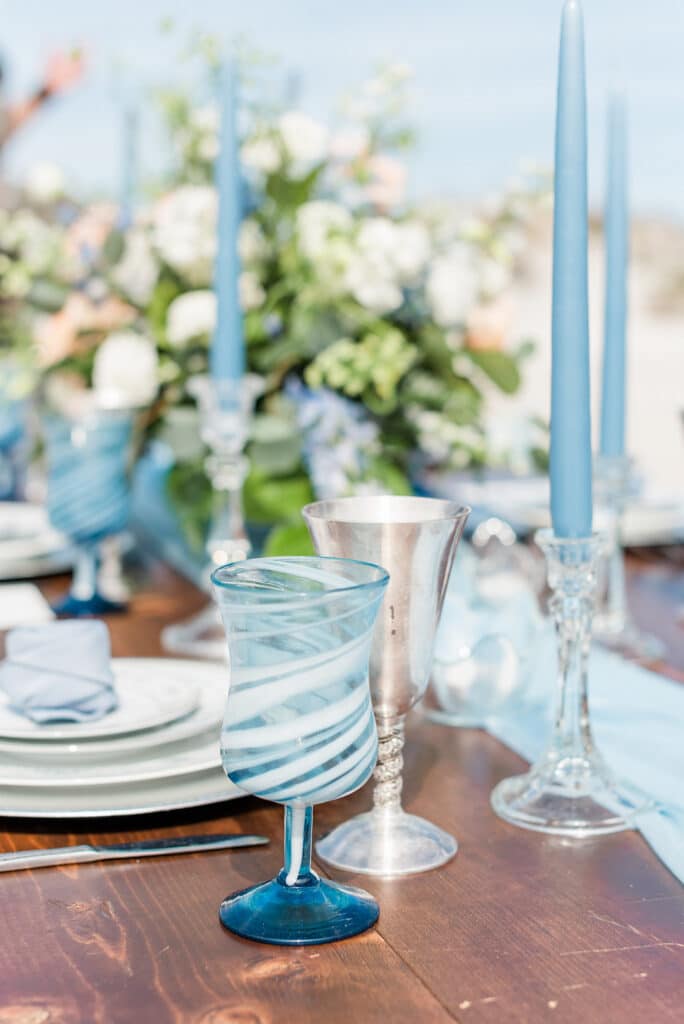 the blue goblets with the stacked plates, rose folded naptkin, candles, and flowers in the background