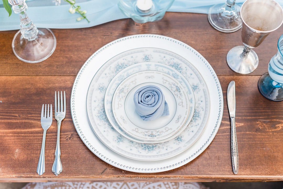the plates stacked on one another with a blue napkin wrapped into a rose in the center