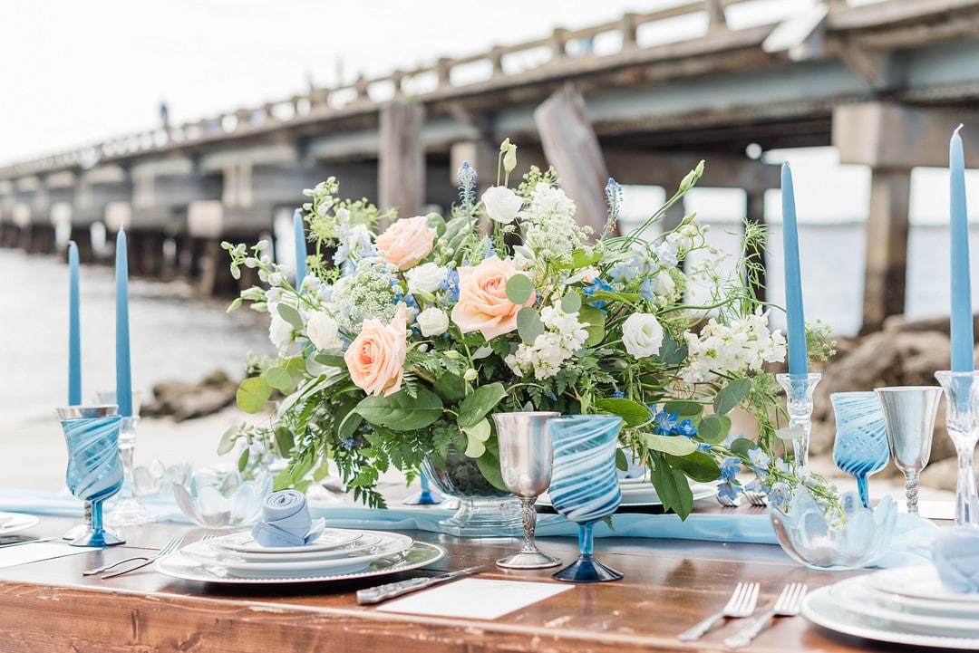 the table center piece surrounded by the blue glasses and the beach in the background