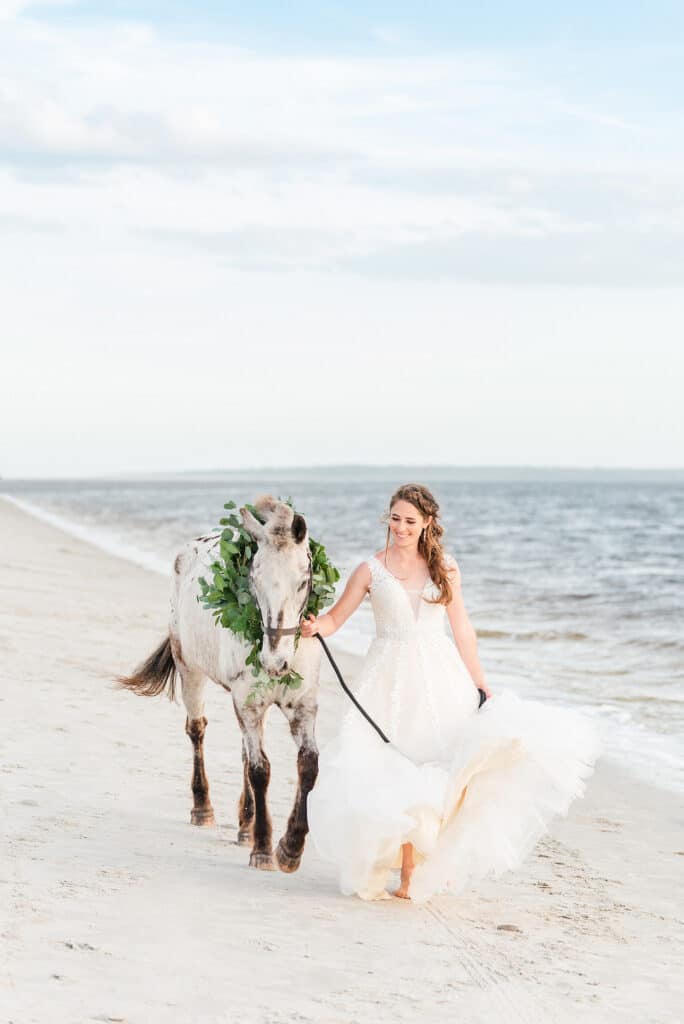 bride and her horse walking down the beach for the amelia island beach wedding inspiration shoot