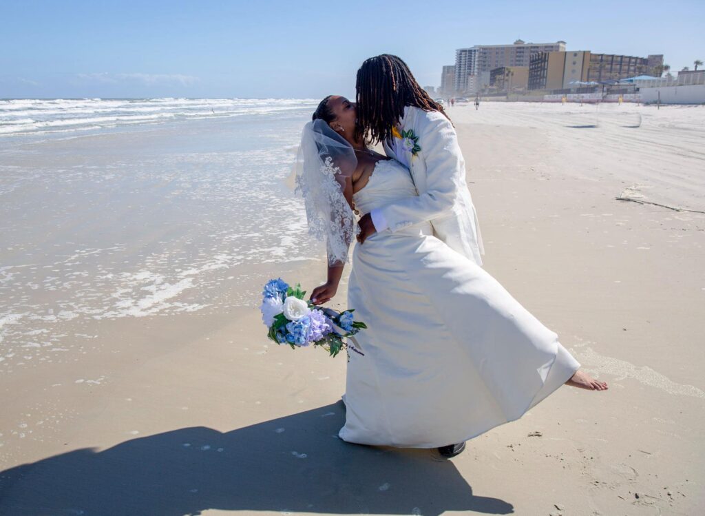 bride and groom kissing on beach while barefoot after wedding ceremony