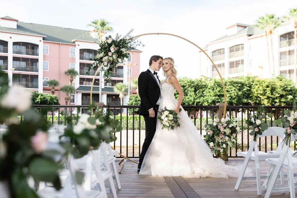 Bride and groom facing the camera under a circular arch. The bride is holding a bouquet of white flowers.