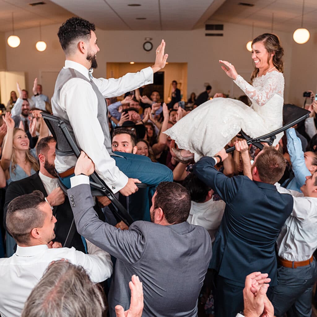 Bride and groom in the air on chairs being held up by guests at a reception