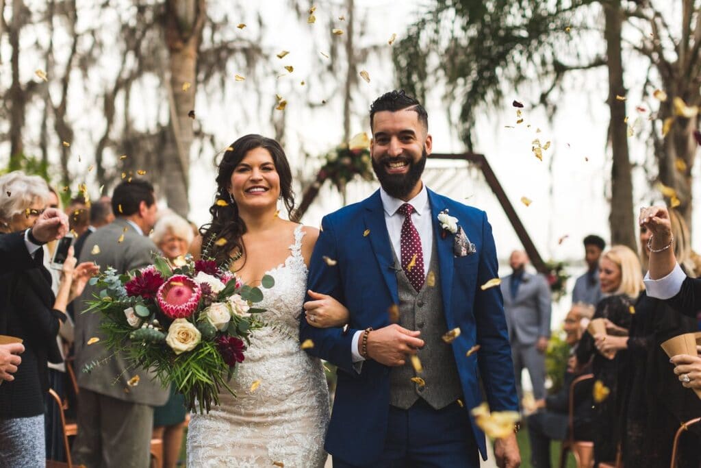 bride and groom smiling after wedding ceremony as guests toss flower petals around them