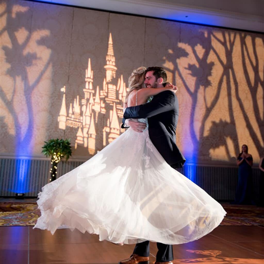 Bride and groom dancing. The groom is lifting the bride off of the floor and there is a projection of a castle in the background.