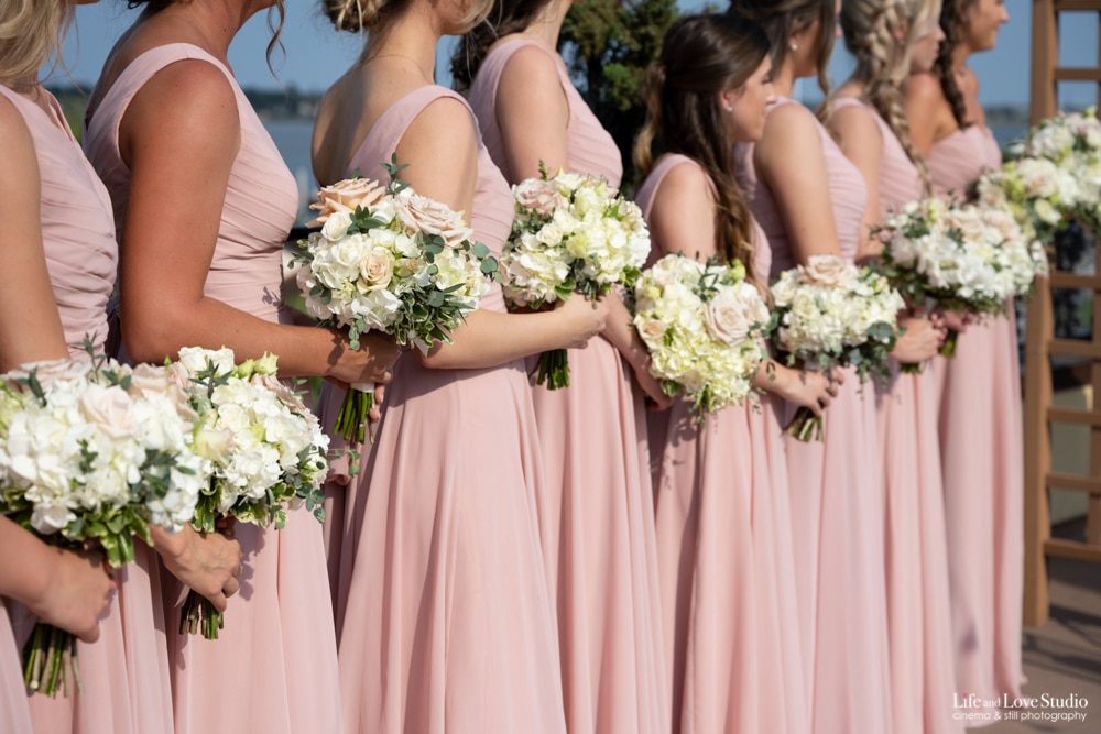 Bridesmaids in petal pink dresses holding bouquets of white and pink flowers.