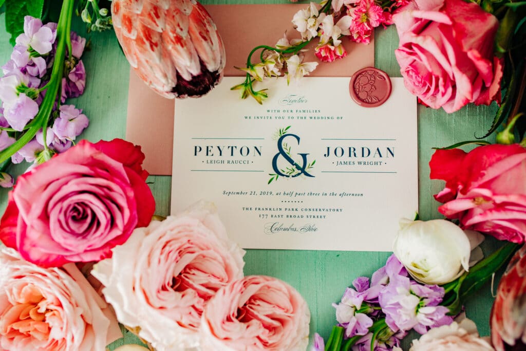 A wedding invitation surrounded by bright colored flowers. It reads 'Peyton and Jordan'.