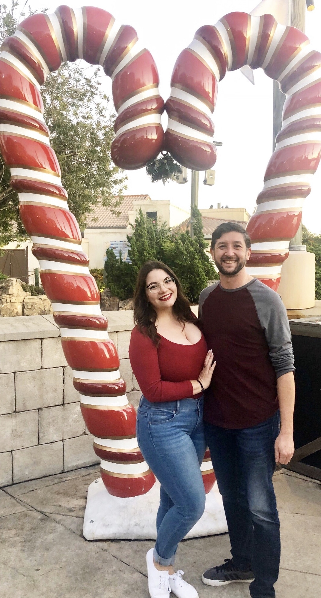 bride and groom to be standing in front of two large candy canes that make a heart, and smiling
