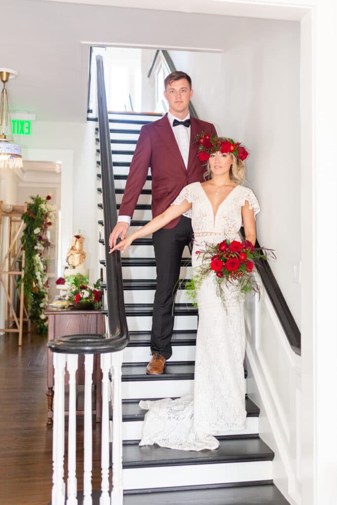 Christmas in July SS 137 - Christmas Themed Wedding Inspiration - Inspiration Shoot bride and groom standing on a stair case wearing red and green accents to match the christmas themed wedding inspiration shoot.