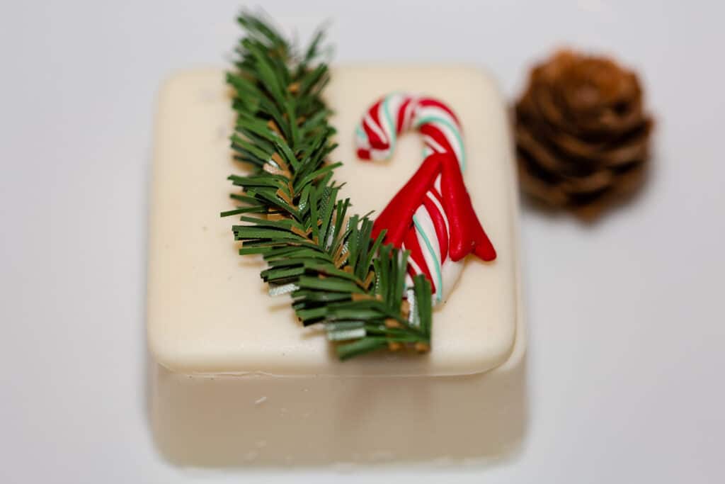Christmas in July SS 149 - Christmas Themed Wedding Inspiration - Inspiration Shoot a white chocolate square decorated with greenery and a small candy cane for Christmas themed wedding inspiration