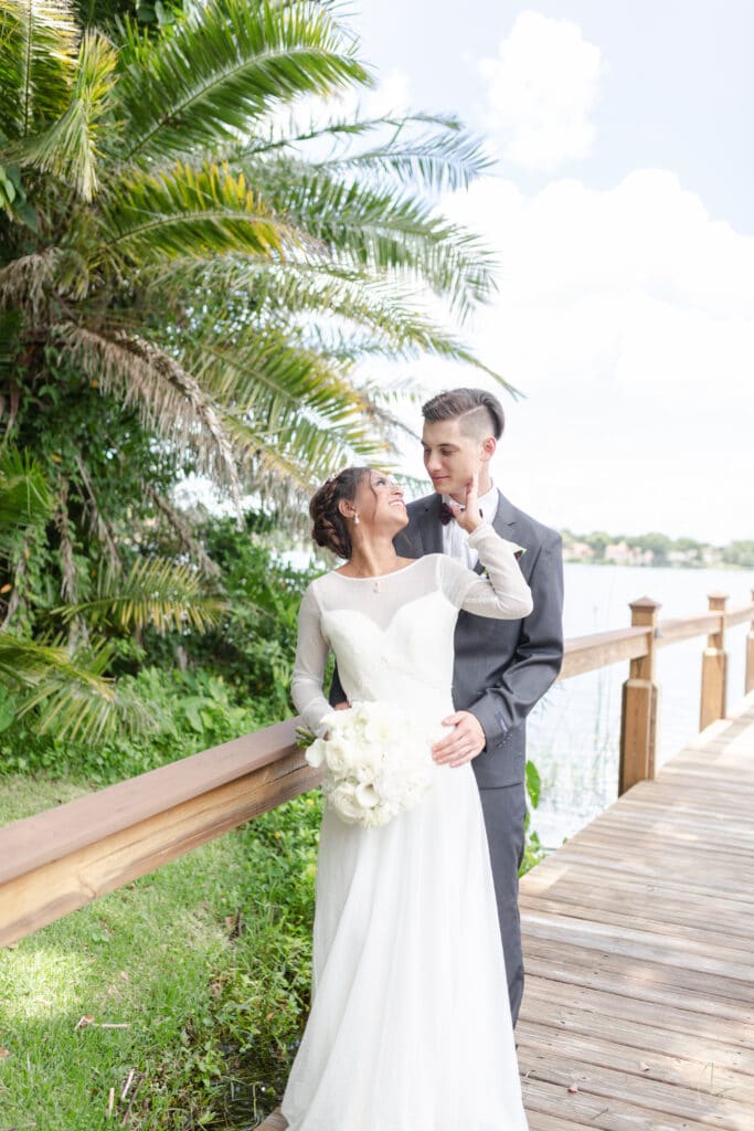 Christmas in July SS 157 - Christmas Themed Wedding Inspiration - Inspiration Shoot Bride and groom on a dock. The bride is reaching back to touch her new husband's cheek. She holds a bouquet of white flowers.